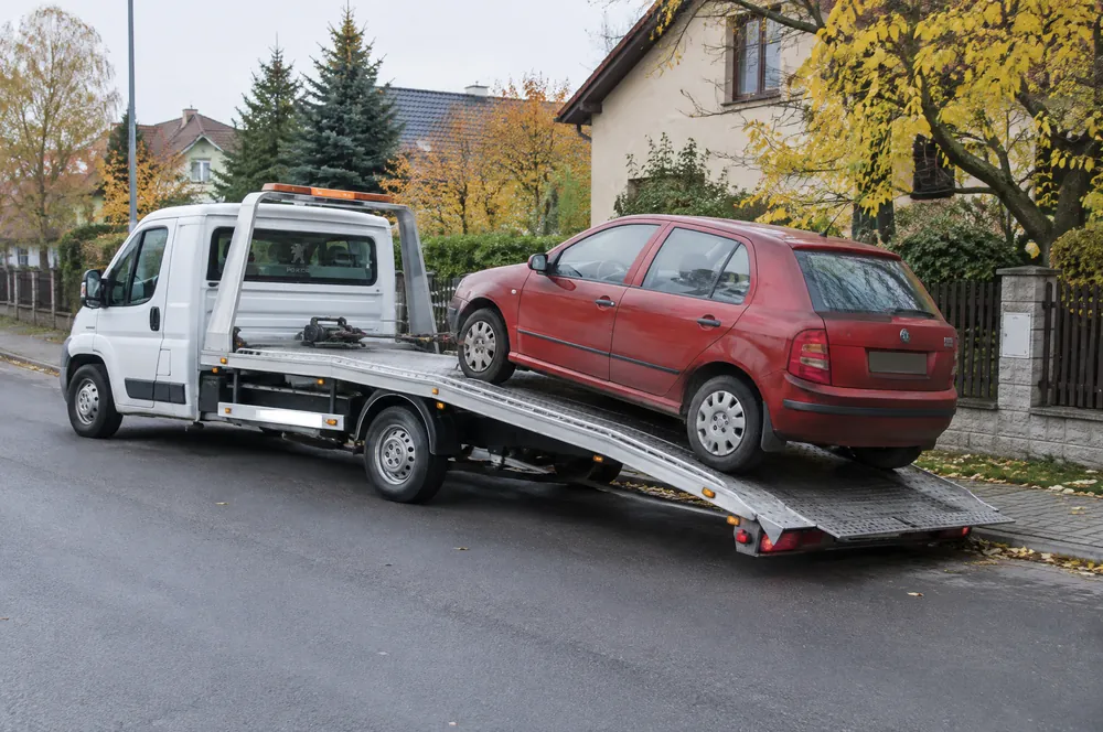 Bílá odtahovka do 3,5 t nakládá červenou Škodu Fabii v ulici rodinných domů v Horních Počernicích